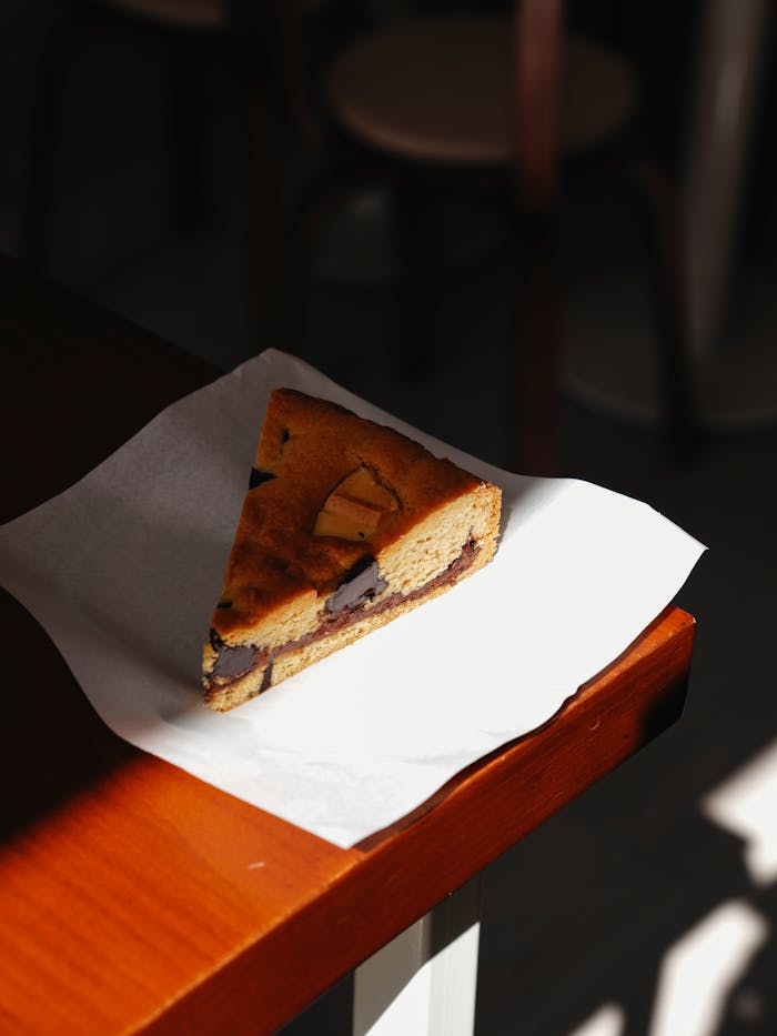 about-02 A single slice of chocolate chip cookie cake on a napkin under warm lighting.
