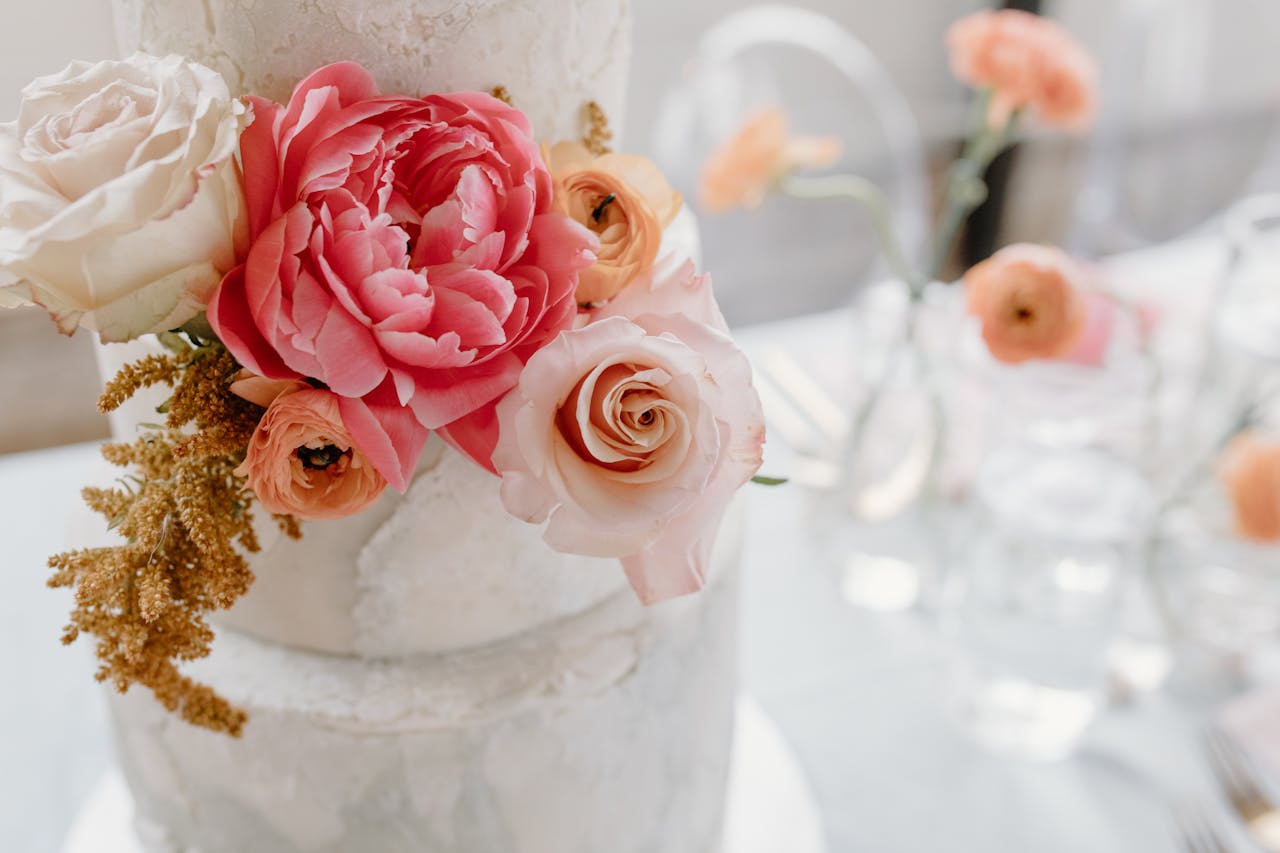 A beautifully decorated wedding cake adorned with pink and white roses and peonies, perfect for a romantic celebration.